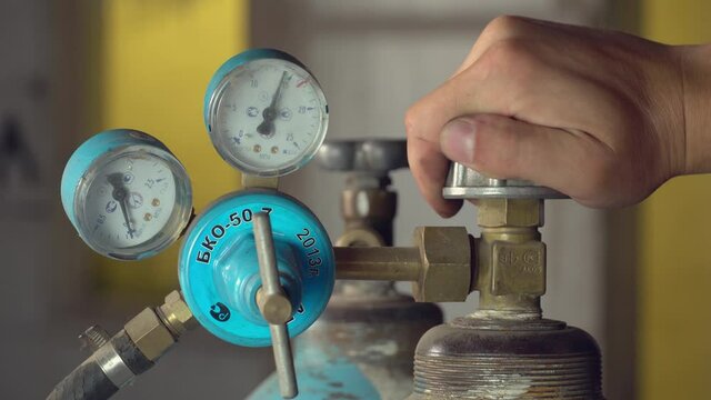 Welding equipment cylinder with acetylene gas, cylinder with pressure regulators, pressure gauges. The man's hand unscrews the tap or valve of the oxygen cylinder.