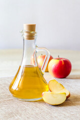 Apple cider vinegar in a glass bottle on a light background with red apples. Malic acid is...