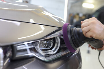 Master repairman polishing headlights of car in workshop using machine closeup