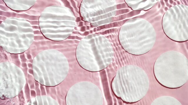Multiple waves of water cross each other creating ripples spontaneously on pale pink background with cotton pads | Background shot for micellar water commercial
