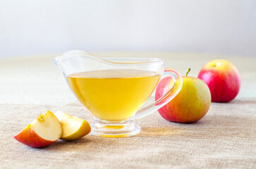 Glass gravy boat with apple cider vinegar and fresh fruits on a light wooden table. Close-up
