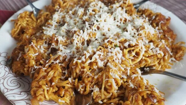 Steaming hot cheese maggi  noodles served in a glass plate with disposable forks served on table in kolkata,india