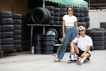 Obraz na płótnie Canvas portrait man and woman skateboarder with sunglasses and fashion pose in front of garage tire