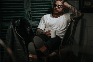 Brutal caucasian hipster holding glass of drink looking to window 