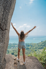Girl looks at the sea near a overlap stone in thailand on the island of koh samui at noon. sunny day and blue beautiful sea with waves