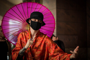 Positive man with dressed in street style clothes red kimono with chains around neck, black panama and black medical mask . Youth and lifestyle concept.