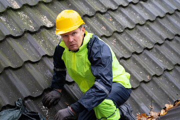 Man builder repairman in yellow helmet makes repairs on the roof