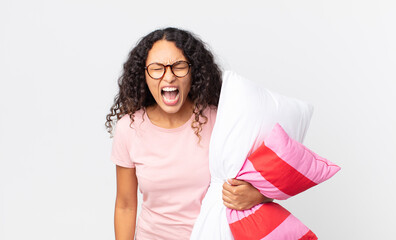 hispanic pretty woman shouting aggressively, looking very angry wearing pajamas and holding a pillow