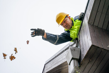 Man builder repairman in yellow helmet makes repairs on the roof