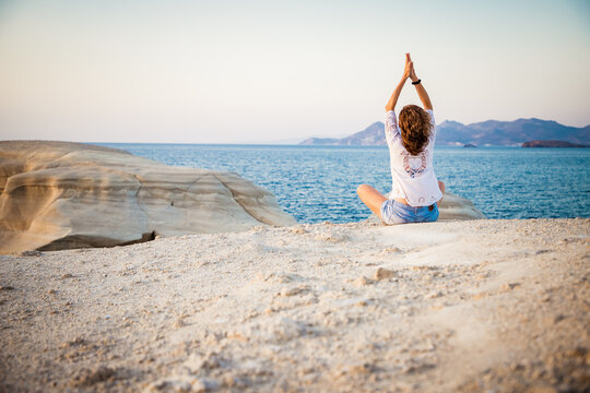 woman in white doing yoga and meditating by the sea