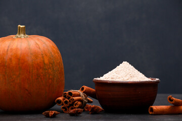 Fresh orange pumpkin, cinnamon, flour in bowl on black table against dark blue wall background....