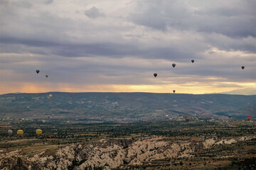 Fototapeta na wymiar Dawn over the valley of Cappadocia. The cloudy sky is highlighted in orange. Colorful balloons are flying over the ground. Turkey