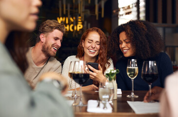 Cheerful friends looking at phone in wine bar