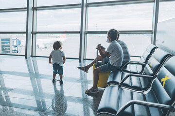 Children at empty airport terminal waiting for departure looking out the window. Little boys in protective medical face mask sits at lounge waiting for plane flight. Family trip concept