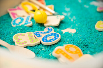 Kid learning numbers through game. Sensory activity with colored rice and wooden numbers. Educations at home, pre-school education, Montessori methodology