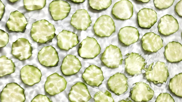 Shot of rippling water surface on white background with cucumber slices in rows | Background shot for skin care cosmetics with vitamin C commercial
