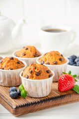 Muffins with chocolate chips on a wooden bord on a white background with fresh berries. Copy space.