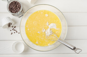 Muffin dough with chocolate chips in a bowl on a white wooden background. Recipe step by step. Top view.