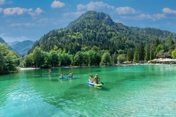 Beautiful landscape of Jasna artificial lake surrounded by forest and people enjoying surfing on a sunny day in Slovenia