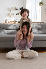 Funny active game at home: young mother give piggyback ride to laughing preschool child. Cheerful...