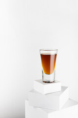 Old golden cognac in shot glass on top of stack of white square podiums, luxury alcohol drink in modern minimal geometric style, soft light space, vertical.