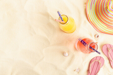 Healthy summer beach vacation on ocean coast - cold pink and orange fruit juice in glass bottles, sun hat, slippers, seashells, top view, copy space.