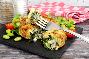 Spinach and kale quiche with fresh salad and edamame beans on a slate serving board