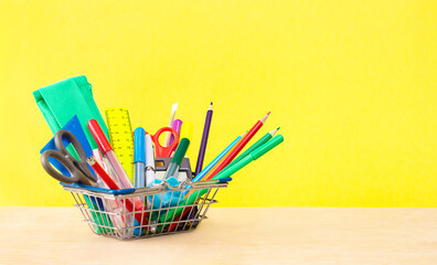 school supplies in a shopping basket on a yellow background