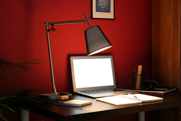 Stylish workplace with modern laptop and glowing lamp in evening