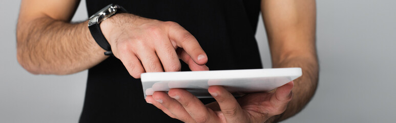 partial view of young man in black t-shirt pointing at digital tablet isolated on grey