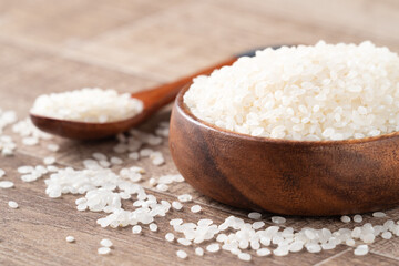Raw white rice in a wooden bowl over table.