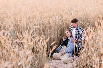 Naklejka na ściany i meble Pregnant young couple enjoys nature on summer evening in field among cereal plants. Family and pregnancy. Love and tenderness. Happiness and serenity. Taking care of new life.