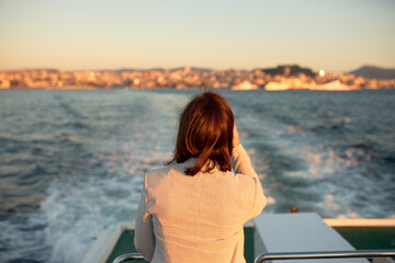 Fototapeta premium Woman with her back on the back of a boat watching as it moves away from the port of the city.