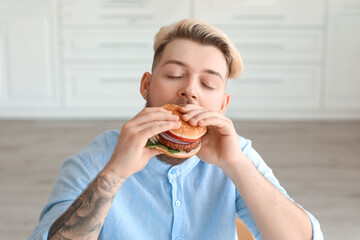 Young man eating vegan burger in kitchen