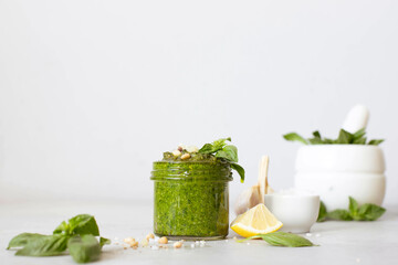 Fresh pesto in a glass jar on a marble table. Olive oil, basil, pine nuts, cheese.