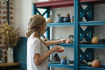 hostess of the ceramic workshop lays out her ceramic dishes on the shelves. feng shui concept....