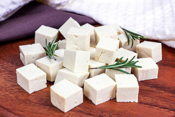 Raw organic vegetarian tofu cubes with fresh rosemary on wooden background.
