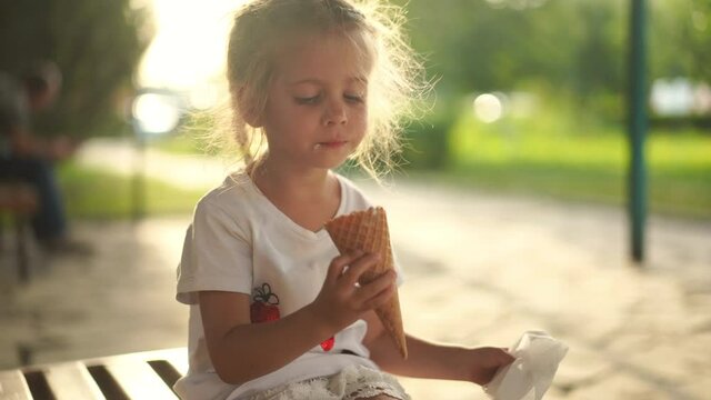 Little girl eat ice cream outdoor. Caucasian female child enjoy while lick white ice cream in waffle cone Summer mood dressed white dress . High quality 4k footage