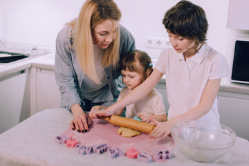 Family makes cookies at home. Mom watches her daughter roll out the dough with a rolling pin.
