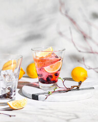 A cold drink with fruit. Summer lemonade with lemon and blueberries. Chiaroscuro from the window. Light and shadows in food photos. Two glasses of a drink with ice on a light background