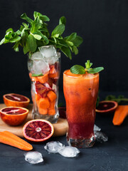 A cold drink on a dark background. Freshly squeezed juice from carrots and red oranges. Serving juice with ice and mint. Fresh fruit and vegetables.