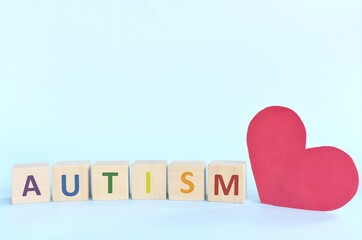 Big red heart shape beside autism letters in wooden blocks typography. Love, support autism spectrum disorder patient.