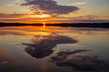 Picturesque morning sunrise with the rising sun and the reflection of colorful sky and clouds on the surface of a a lake in Siikaranta near Suomussalmi, Finland