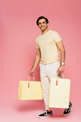 full length of cheerful young man holding shopping bags with sale tags on pink
