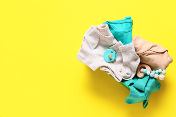 Box with baby clothes, teether and pacifier on color background