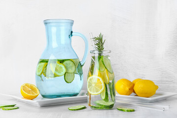 Bottle and jug with cucumber lemonade on light background