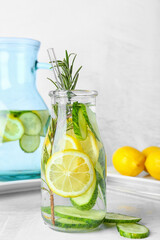 Bottle with cucumber lemonade on light background