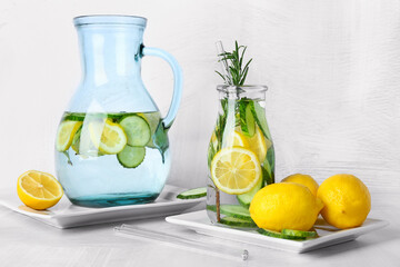 Bottle and jug with cucumber lemonade on light background