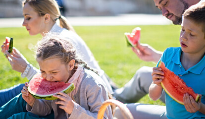 Parents with children, boy and girl eating juicy watermelon at picnic
