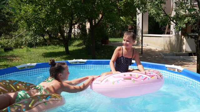 Happy kids fight trying to ride donut floats in outdoor swimming pool on sunny summer day, fun